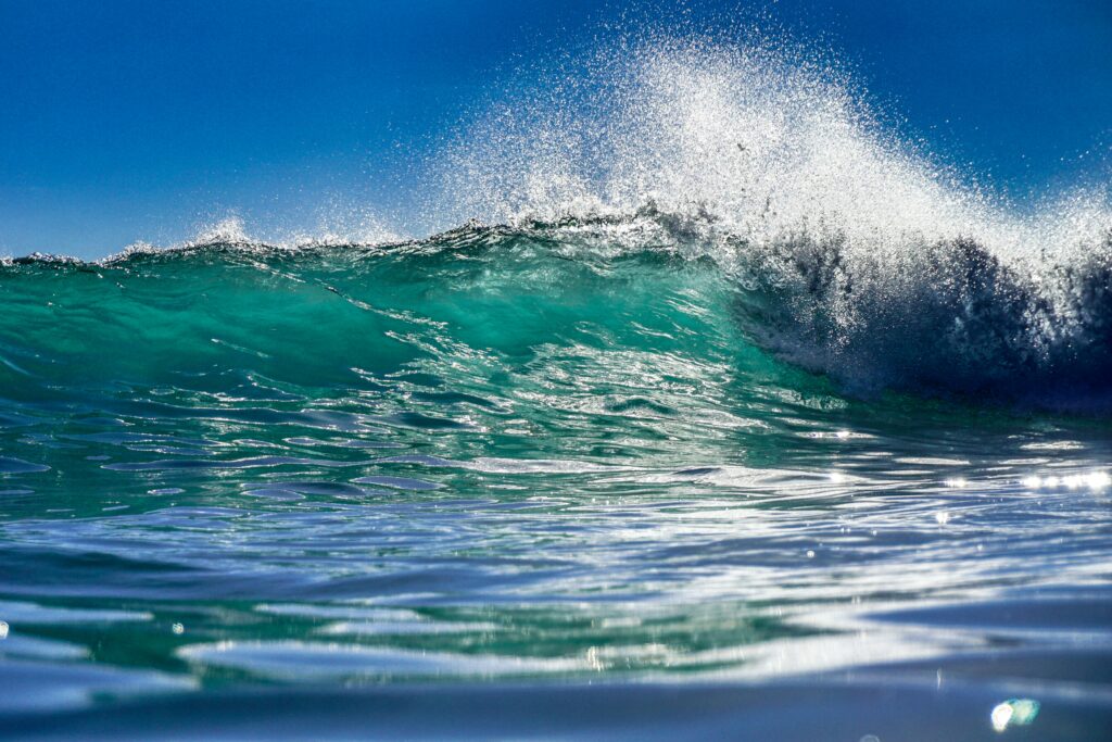 A blue-green ocean wave crests with a blue sky. 